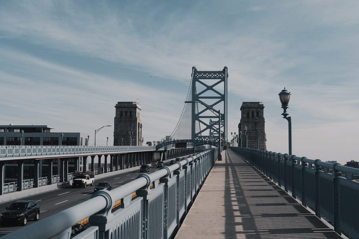 The pedestrian walkway on the Ben Franklin Bridge running toward the tower, with traffic on the roadway alongside