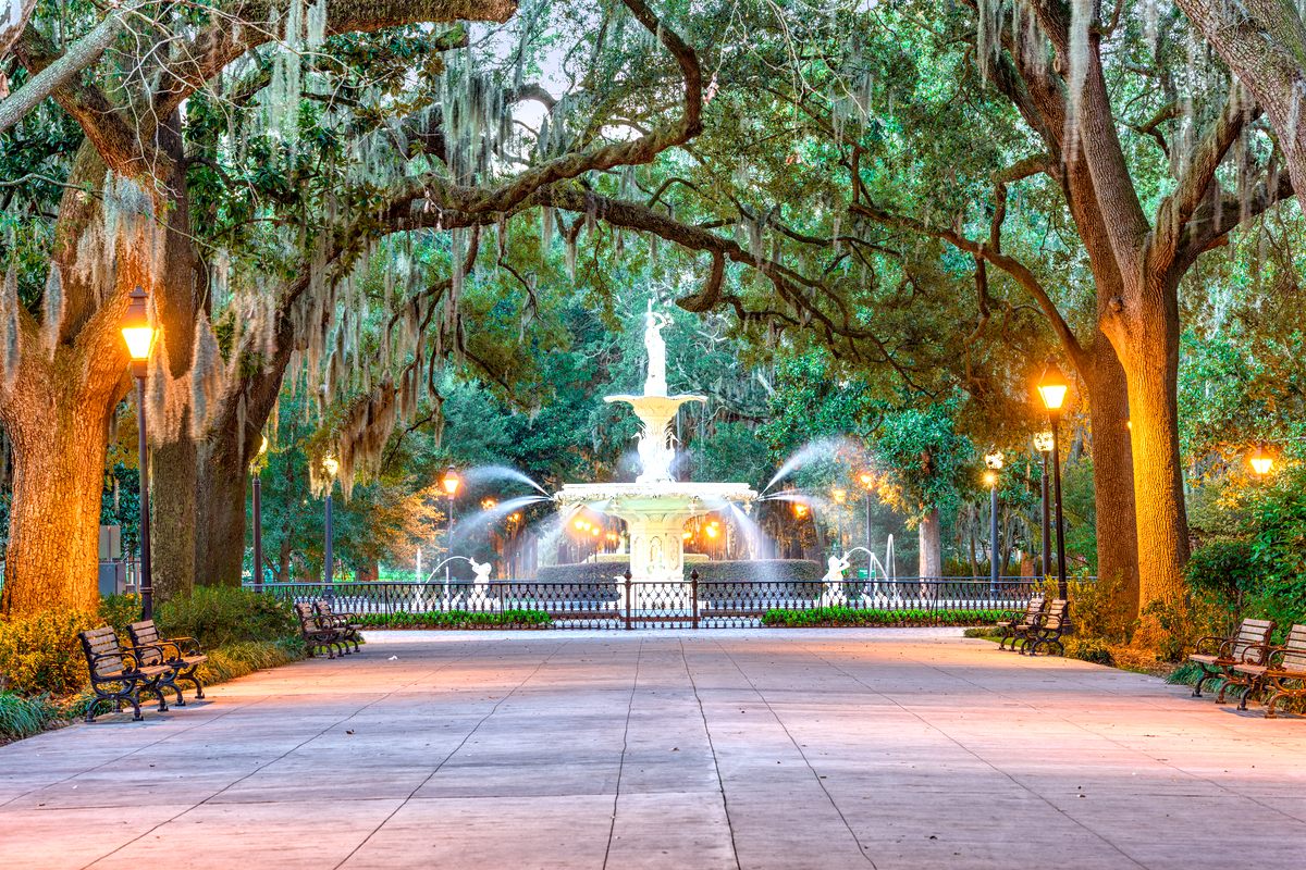 The Forsyth Park fountain in Savannah framed by moss-draped oaks at golden hour, park lamps glowing