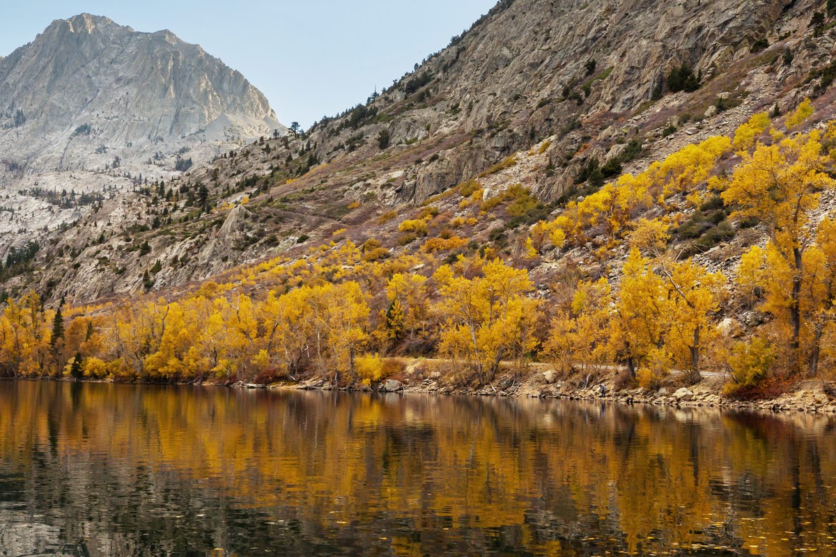 A granite peak above a steep hillside of golden aspen, mirrored in the still lake at its foot