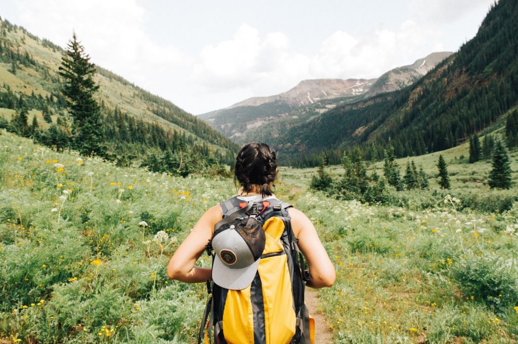 A hiker walks on a grassy path between mountains in Crested Butte