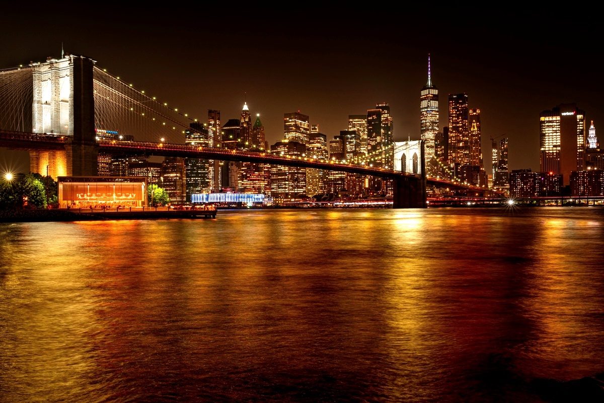 The Brooklyn Bridge lit warm gold at night with the Manhattan skyline rising behind it