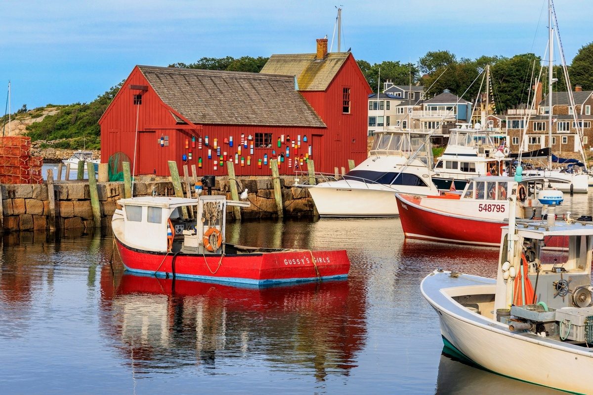 The red fishing shack Motif No. 1 on Rockport harbor, lobster buoys on its wall and boats moored on calm water