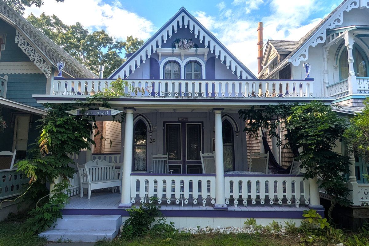 A lavender gingerbread cottage in Oak Bluffs with white fretwork trim and white rocking chairs on its front porch