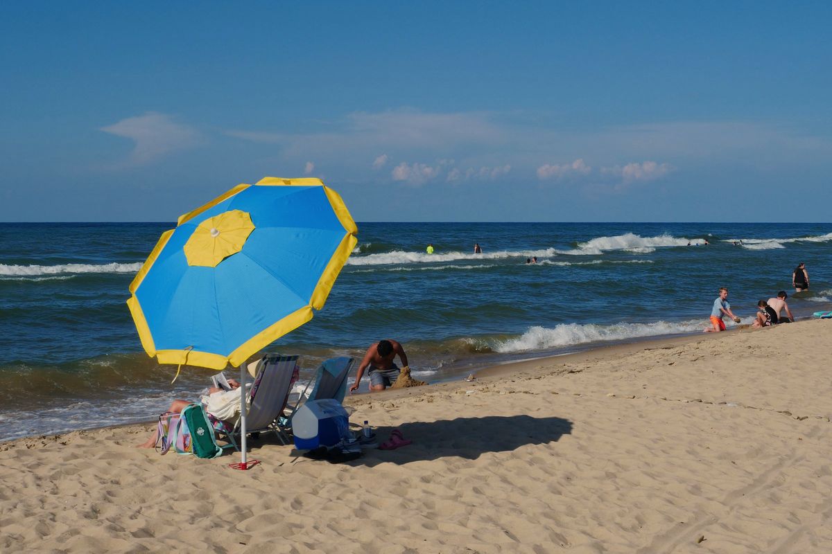 A blue and yellow beach umbrella on the sand at Indiana Dunes, with swimmers in the Lake Michigan surf behind it
