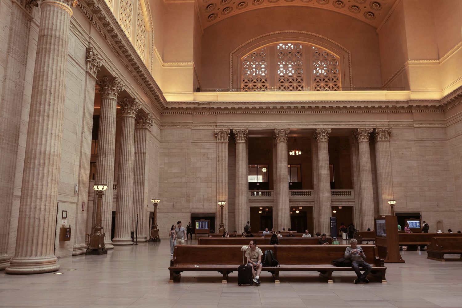 The Great Hall of Chicago Union Station, travelers waiting on the long wooden benches beneath the skylight and columns