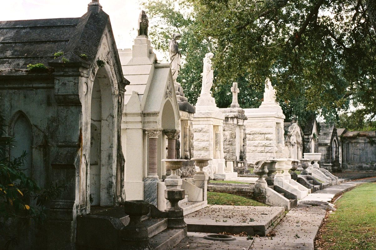 Ornate above-ground tombs lining a path through a historic New Orleans cemetery on a bright afternoon