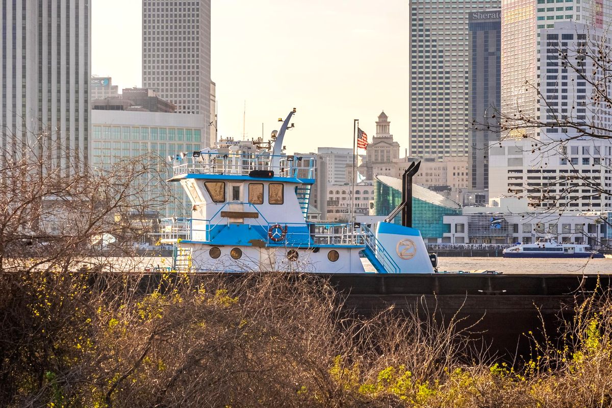 A blue and white tugboat working the Mississippi River wharf in front of the downtown New Orleans skyline
