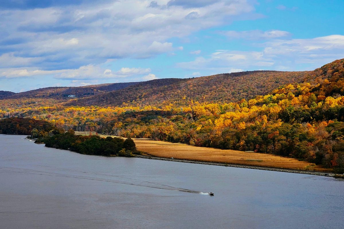The Hudson River at Cold Spring, New York, in the fall, with orange and gold hills along the far bank and a small boat crossing the water