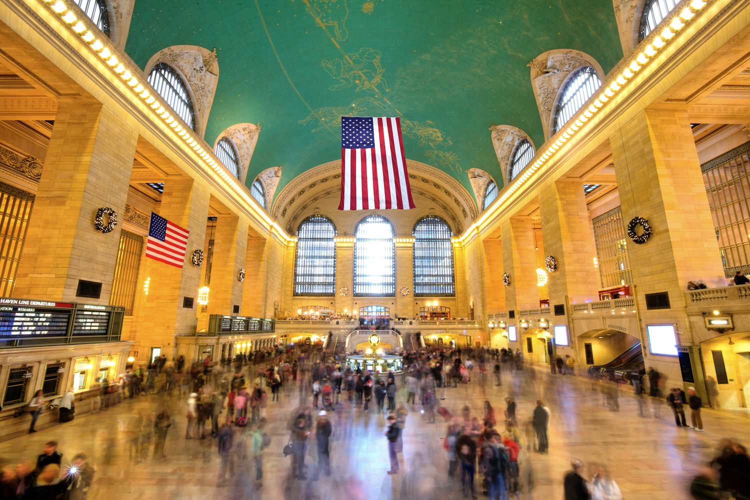 The main concourse of Grand Central Terminal, with American flags hanging beneath the green celestial ceiling and travelers crossing the marble floor