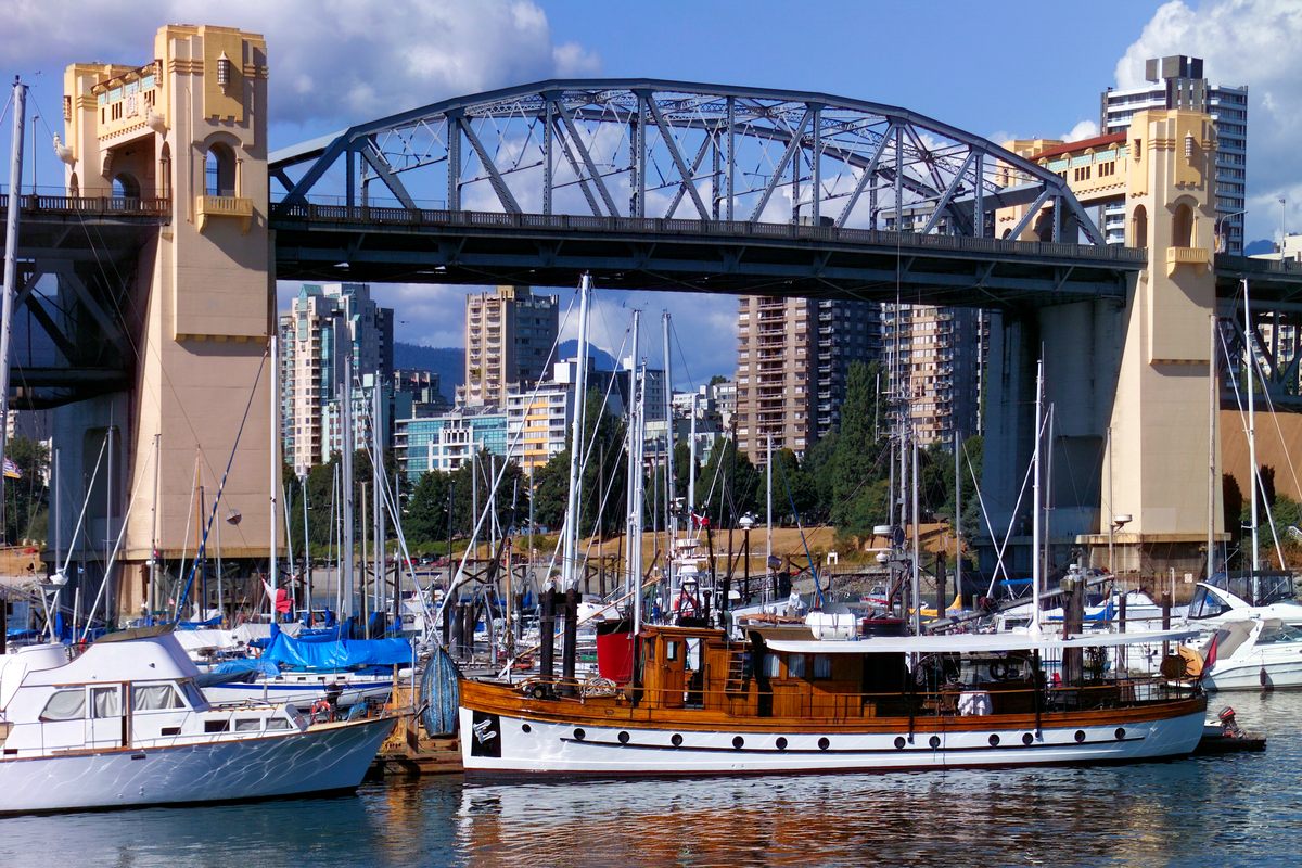 Sailboats and a wooden cruiser moored in the False Creek marina in Vancouver, BC, under the steel truss of the Burrard Bridge, with apartment towers behind