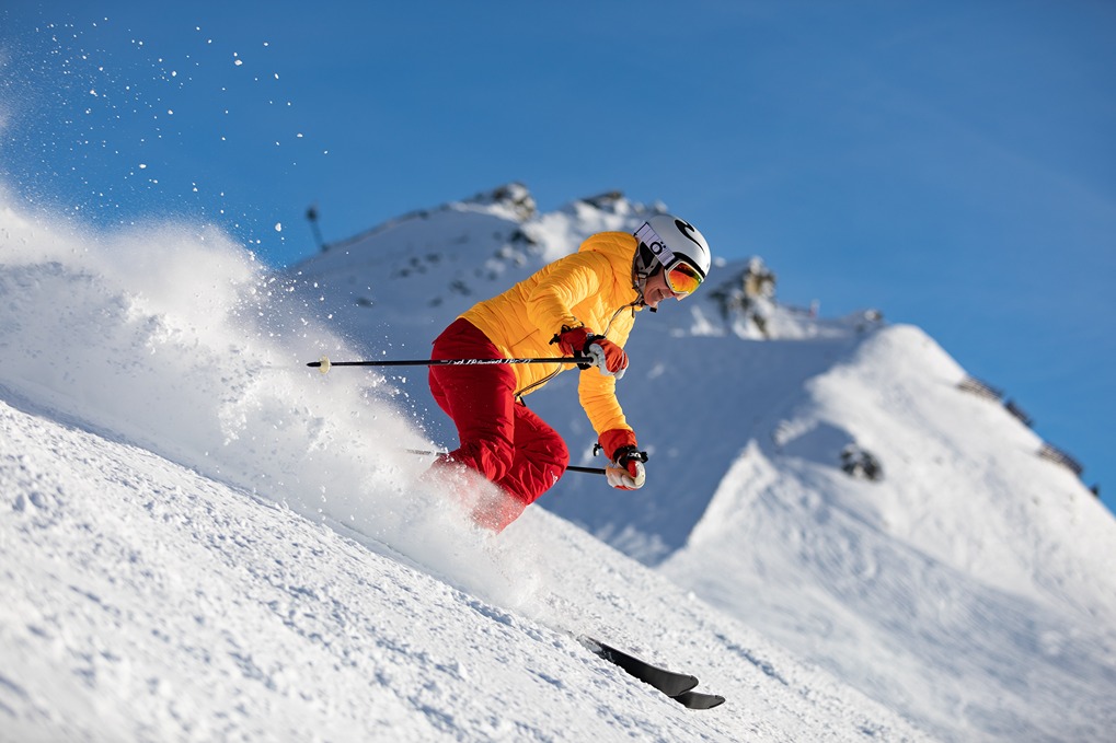 A person wearing bright yellow and red snow gear skis down a snow-covered mountain in New Hampshire